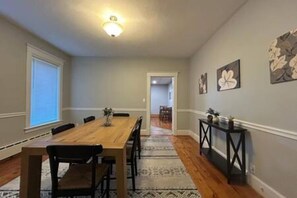 Un comedor con mesa y sillas de madera, un tapete estampado y decoración en la pared.
