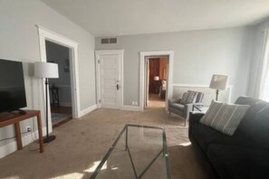 A living room with a TV, a glass coffee table, a sofa, and a lamp.