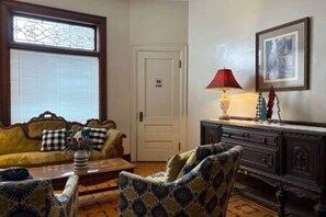 Una habitación con sofá, sillón y un armario. Se observa una puerta con un número.