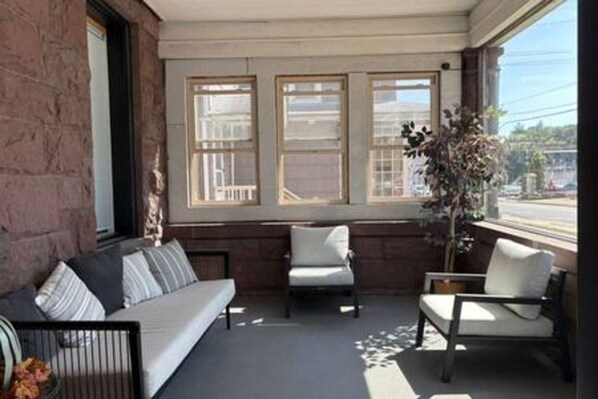 A room with a built-in bench, two chairs, a potted plant, and a window with a view.