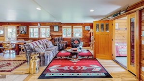 L’intérieur chaleureux d’un chalet en bois comprend un coin repas, un salon avec un canapé et des fauteuils, ainsi qu’une grande fenêtre.