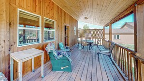 A wooden deck with a table and chairs, a covered area with a table and chairs, and a view of a house in the background. - 3BR Rustic Cabin w/ 2 Decks & Hot Tub (Garden Valley)