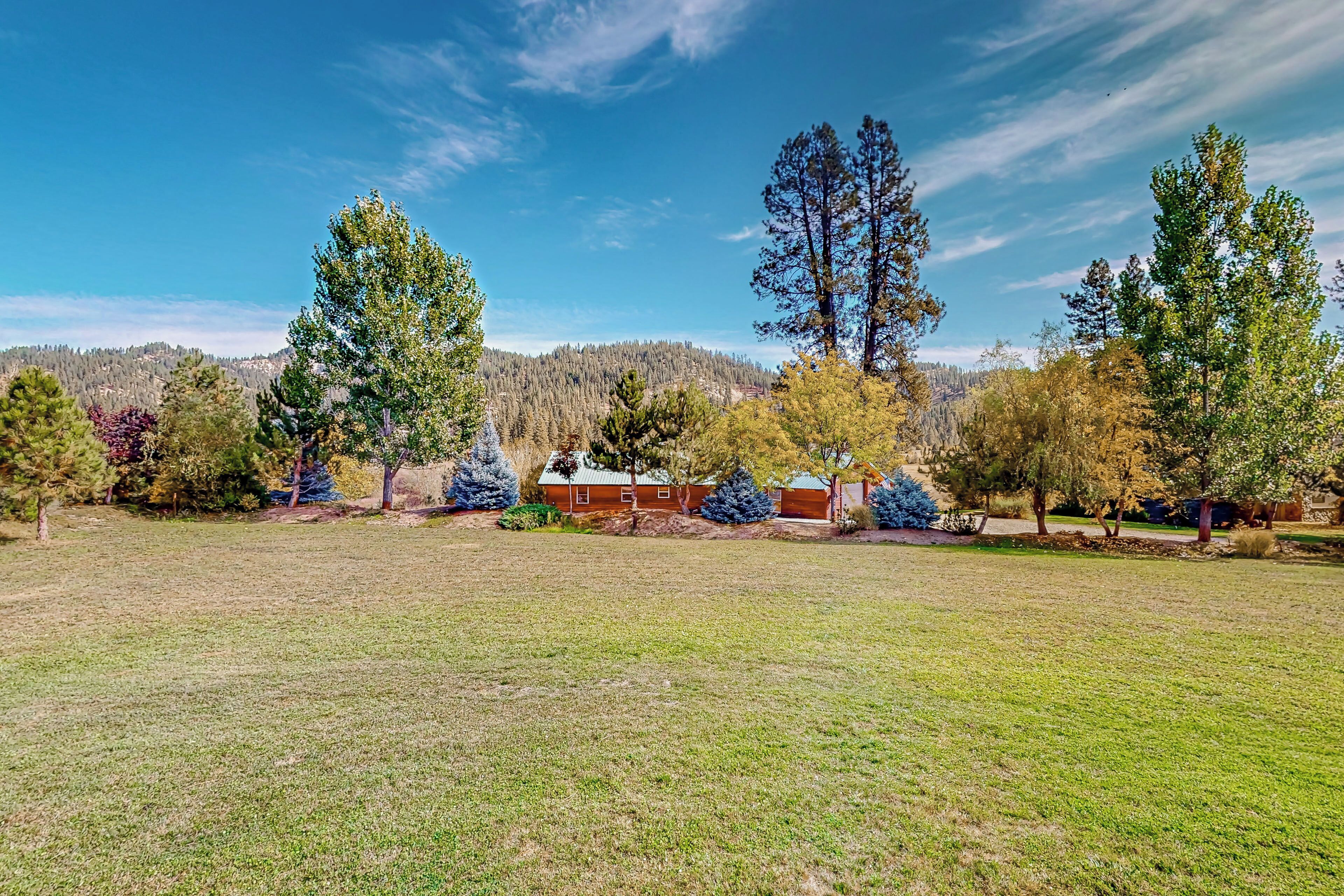 A spacious grassy field with a house and several trees in the background.