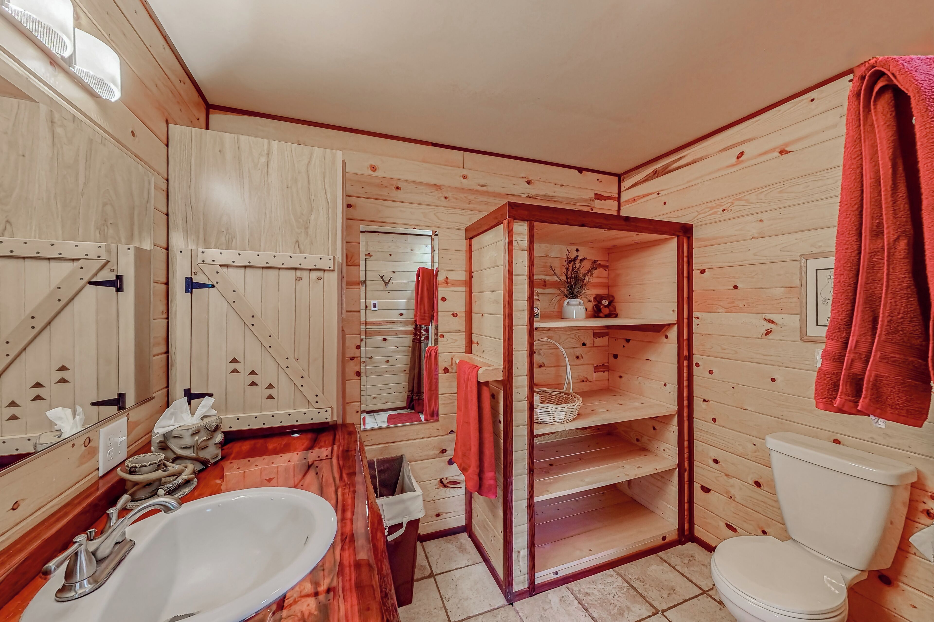 Une salle de bain rustique, avec des murs en bois, comprenant un lavabo blanc, des toilettes et un miroir.