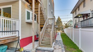 En bostadsbyggnad med en trätrappa som leder upp till en veranda, en inhägnad trädgård och en asfalterad gångväg.