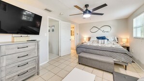 A bedroom with a bed, a TV, a ceiling fan, and a wall with a 'love' sign. - Beach Time + Pool Vibes! Port Charlotte Hideaway (Port Charlotte)