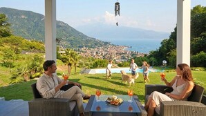 A terrace with wicker furniture, a pool, and a view of a coastal town. - D1MORA Sophie - exclusive privacy with view & pool (Salò)