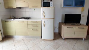 Uma cozinha compacta com fogão, micro-ondas, frigorífico e uma televisão sobre um móvel.