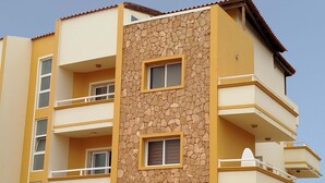 Um edifício de vários andares com varandas, fachada de pedra e telhado plano.
