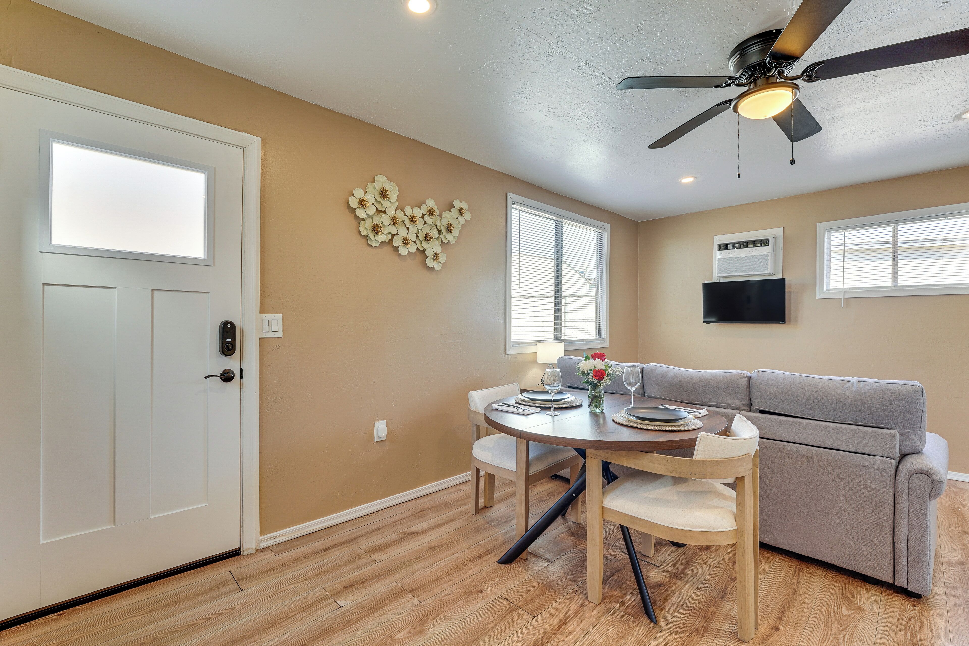 A dining area with a round table, chairs, a grey sofa, and a ceiling fan.