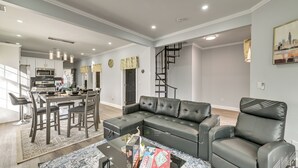 A modern living room with a sectional sofa, a dining area with a kitchen in the background, and a staircase leading to an upper floor. - Walk to Park: Modern Apt 2 Mi to Union College! (Schenectady)