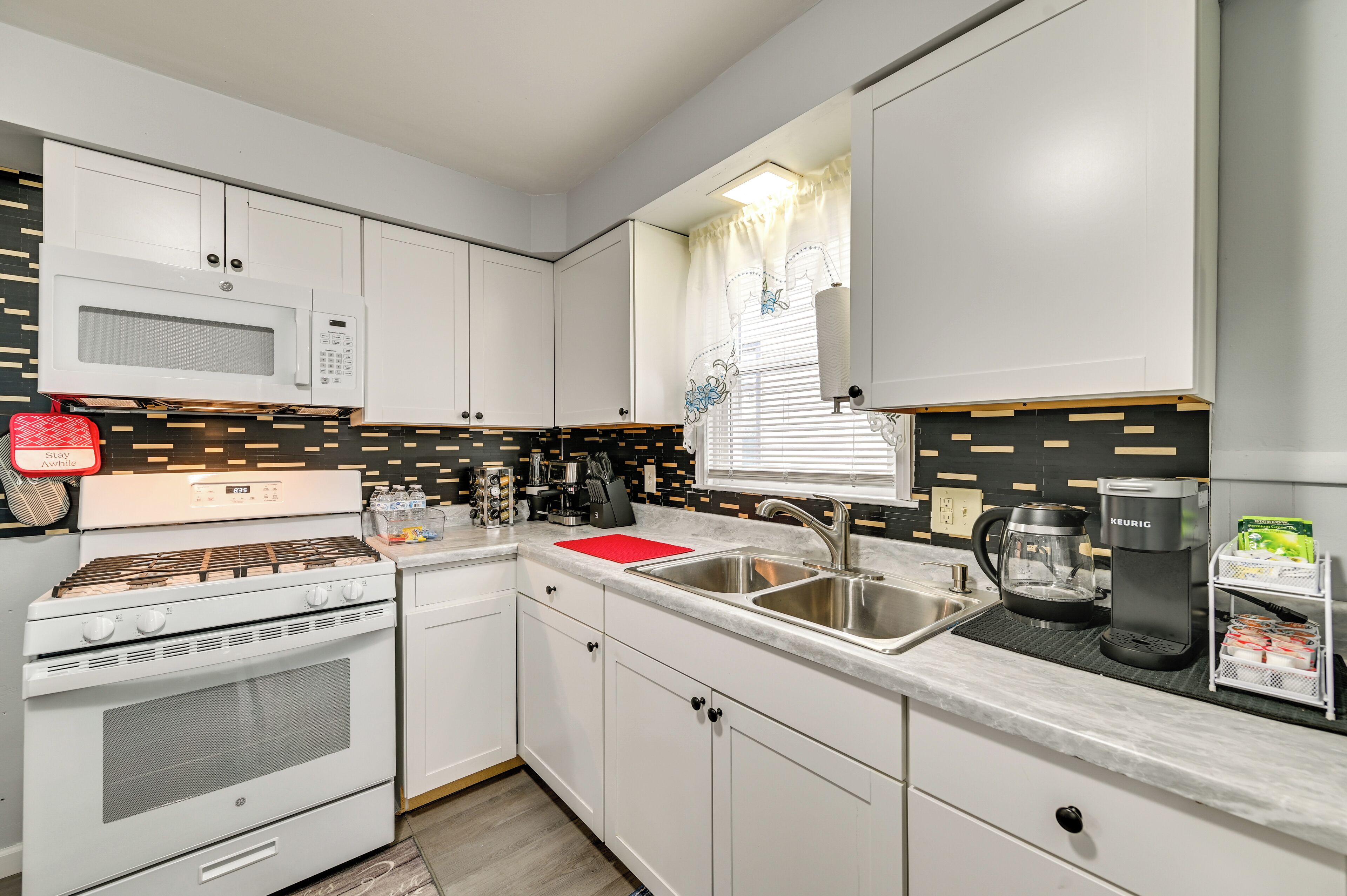 A modern kitchen with white cabinets, a built-in microwave, a gas stove, a coffee maker, and a sink.