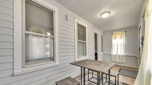 Ein Zimmer mit Holztisch und Bänken, großen Fenstern mit Vorhängen und einem Deckenventilator.