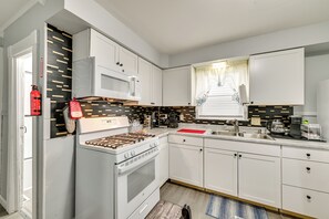 Ett modernt kök med vita skåp, en gasspis, en mikrovågsugn och en röd skärbräda.