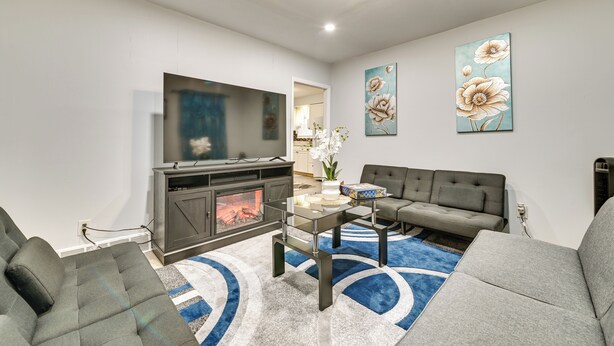Ein modernes Wohnzimmer mit Kamin, Flachbildfernseher, grauen Sofas und abstrakter Blumenkunst an der Wand.