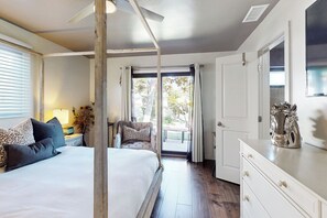Une chambre avec un grand lit, une table de chevet avec une lampe, une chaise et une vue sur l’extérieur grâce à une porte vitrée.