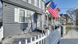 Une maison à deux étages avec un porche à l’avant, un drapeau et une clôture blanche en bois.