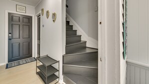 Un escalier avec une rampe et une porte sombre surmontée d’un paillasson.