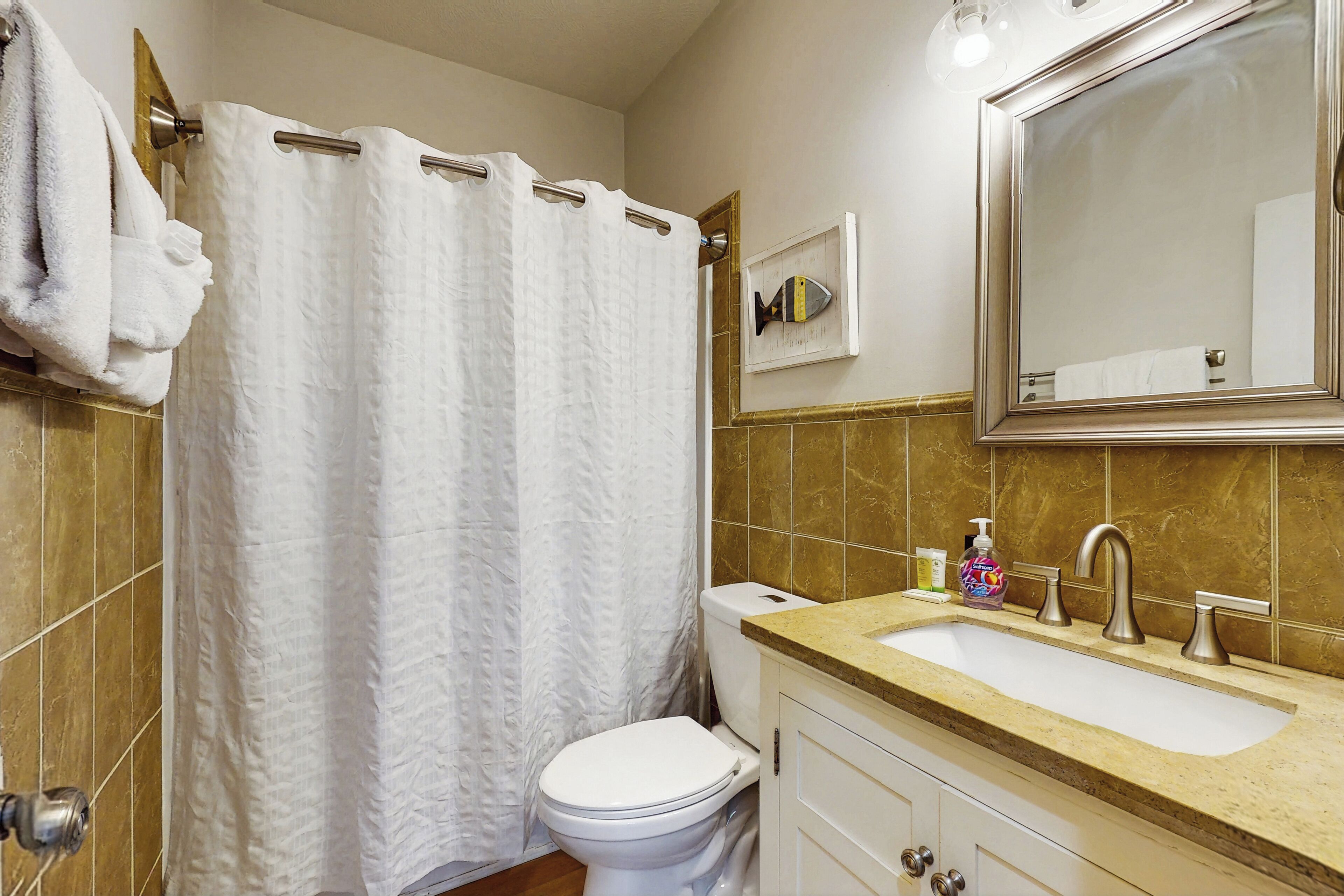 Un baño con inodoro blanco, un lavamanos color beige con espejo y cortina de ducha.