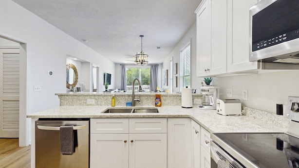 A modern kitchen with white cabinetry, a stainless steel dishwasher, a built-in oven, and a large microwave. - 2BR Condo on Golf Course w/ Pool & Tennis Court (Myrtle Beach)