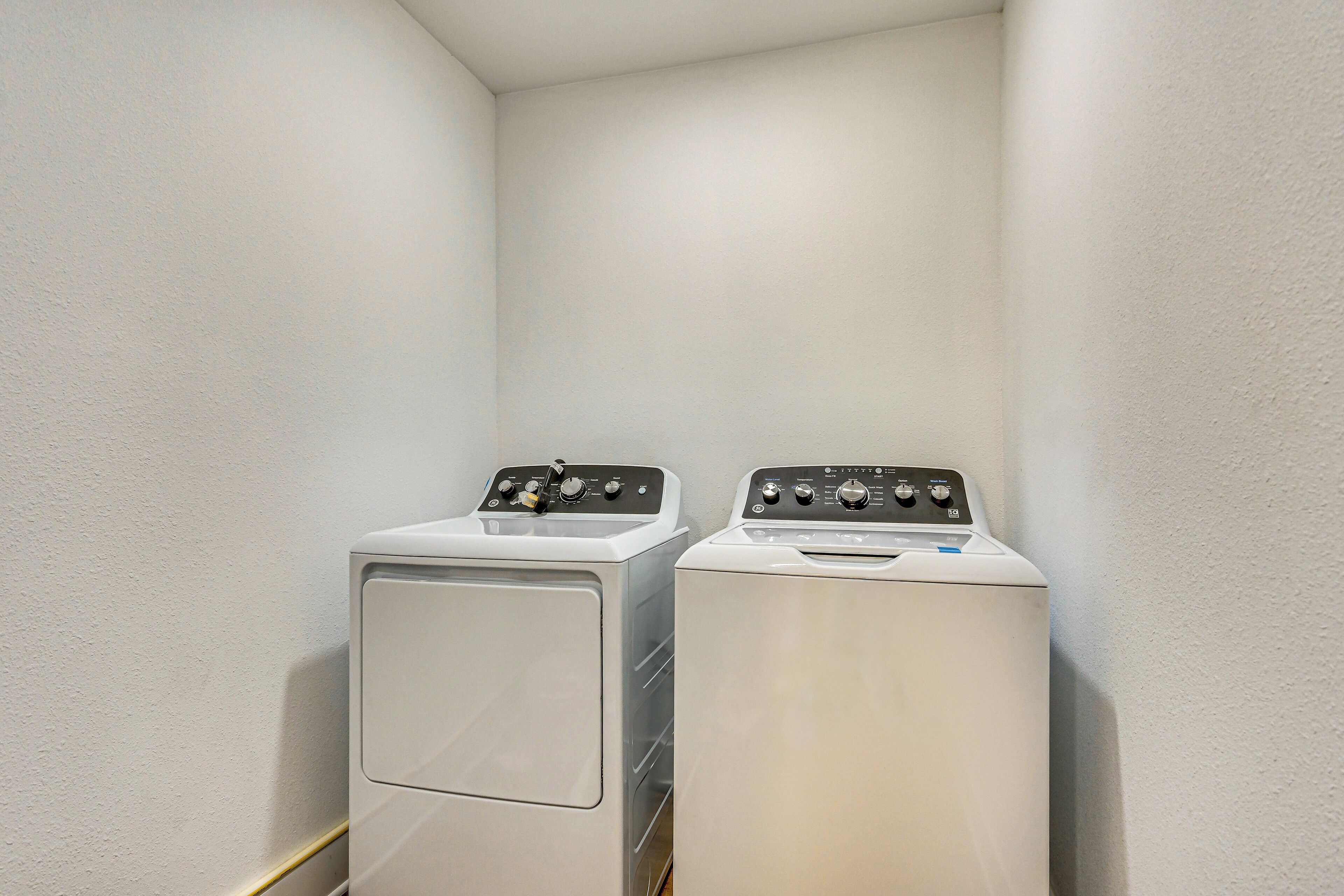Two front-loading washing machines in a corner of a room with plain walls.