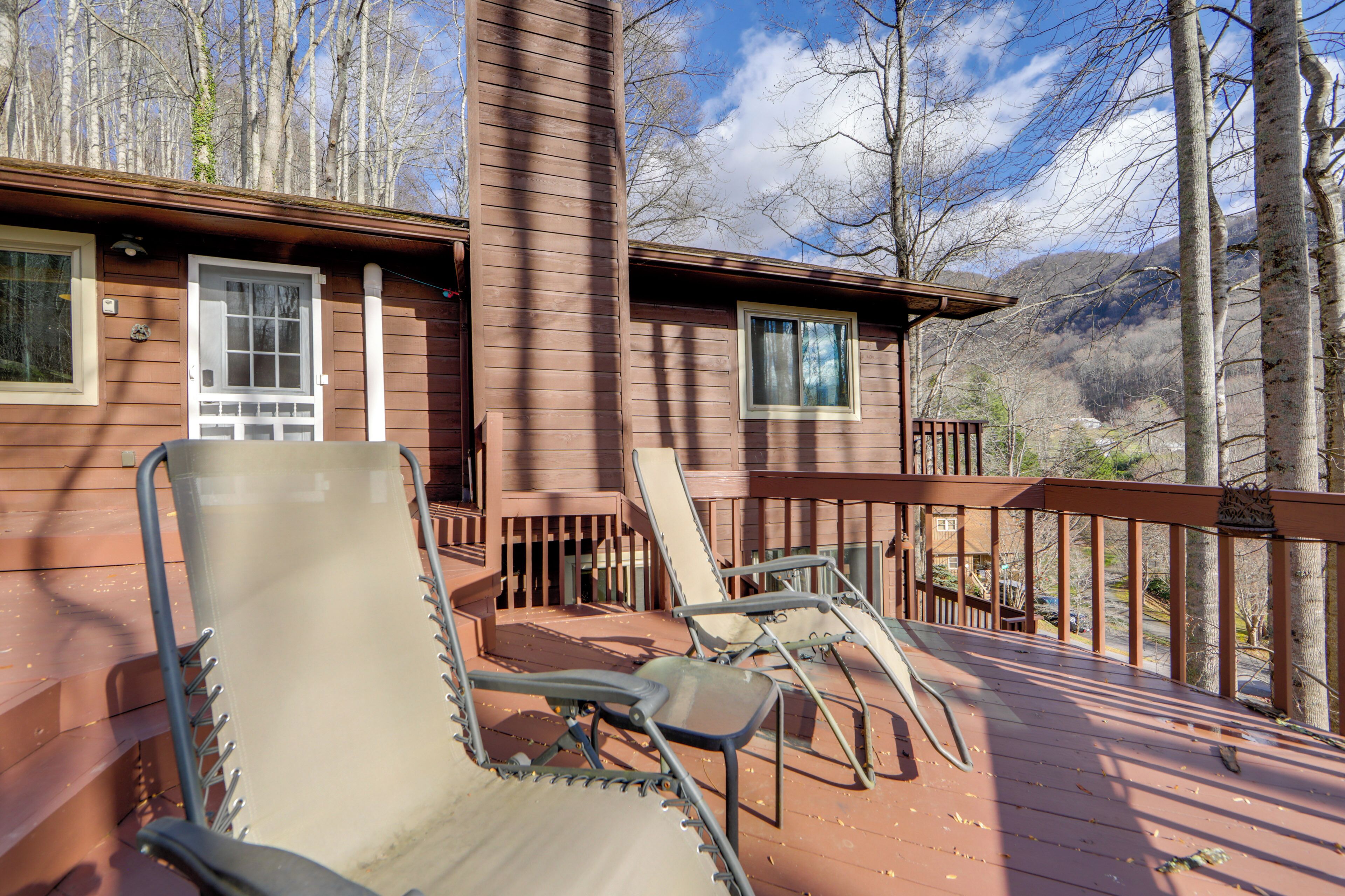 A wooden deck with two lounge chairs and a small table, overlooking a mountainous landscape.