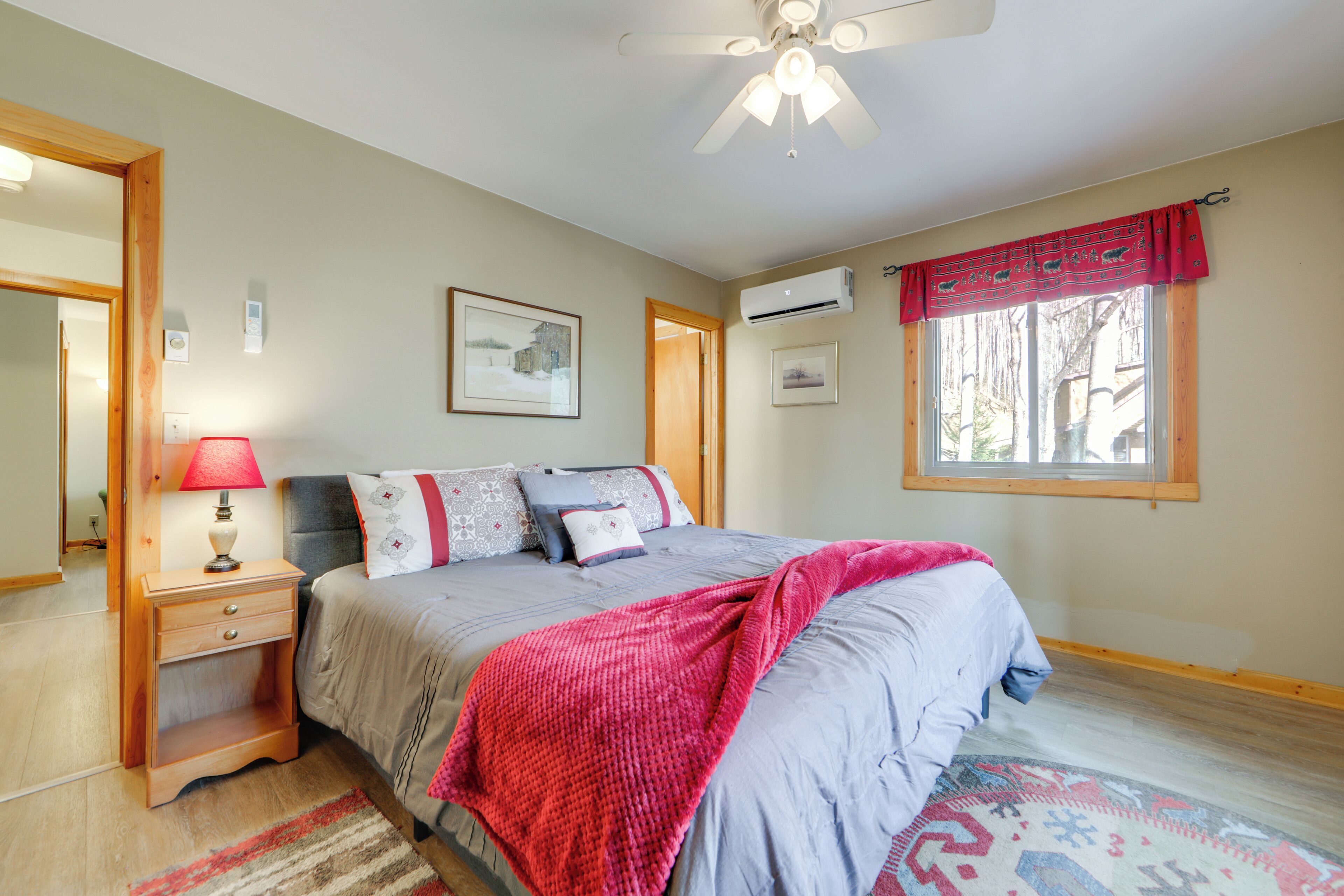A bedroom with a bed, bedside table, lamp, ceiling fan, and window with curtains.