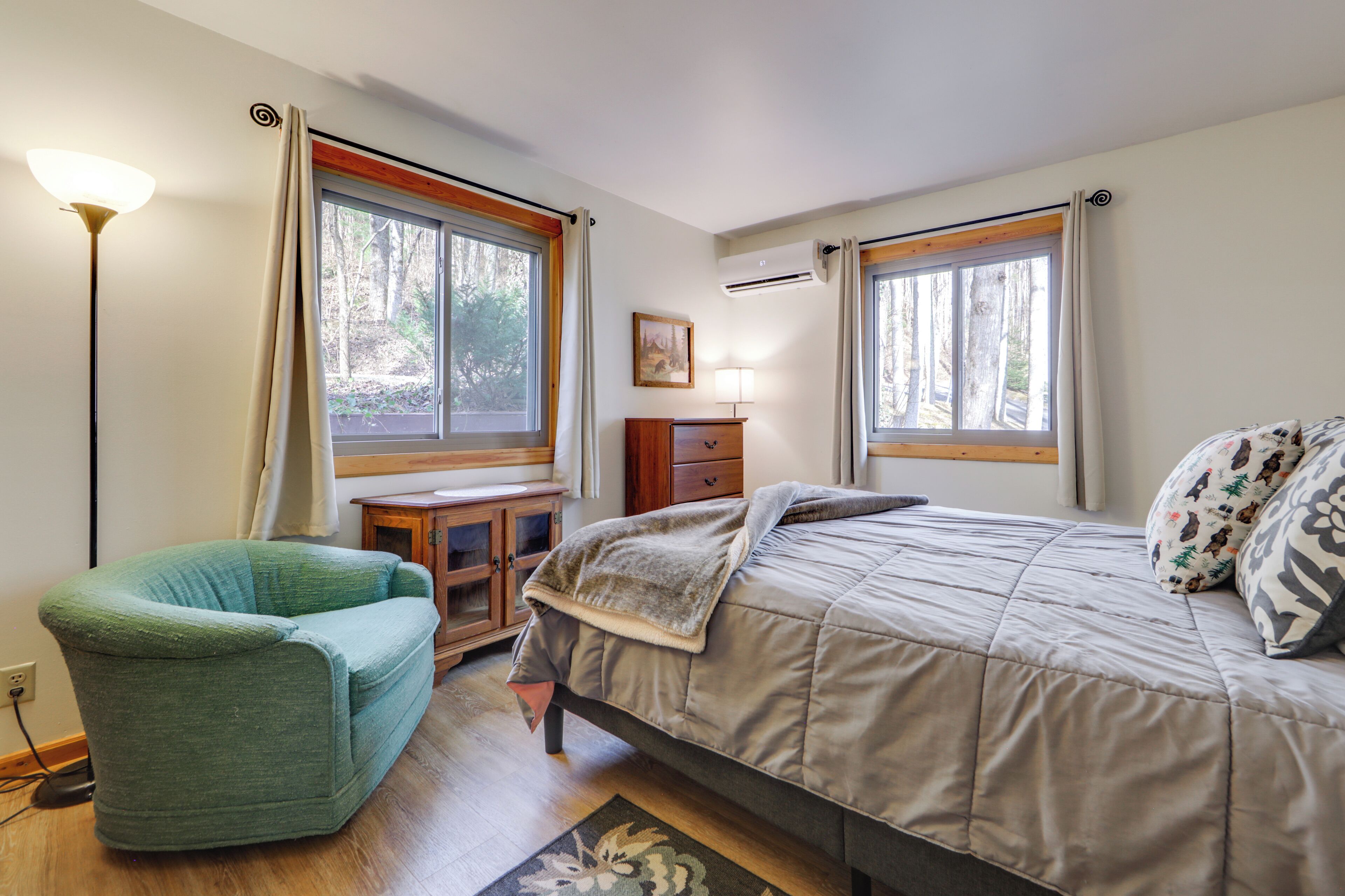 A bedroom with a bed, a chair, a dresser, and two windows.