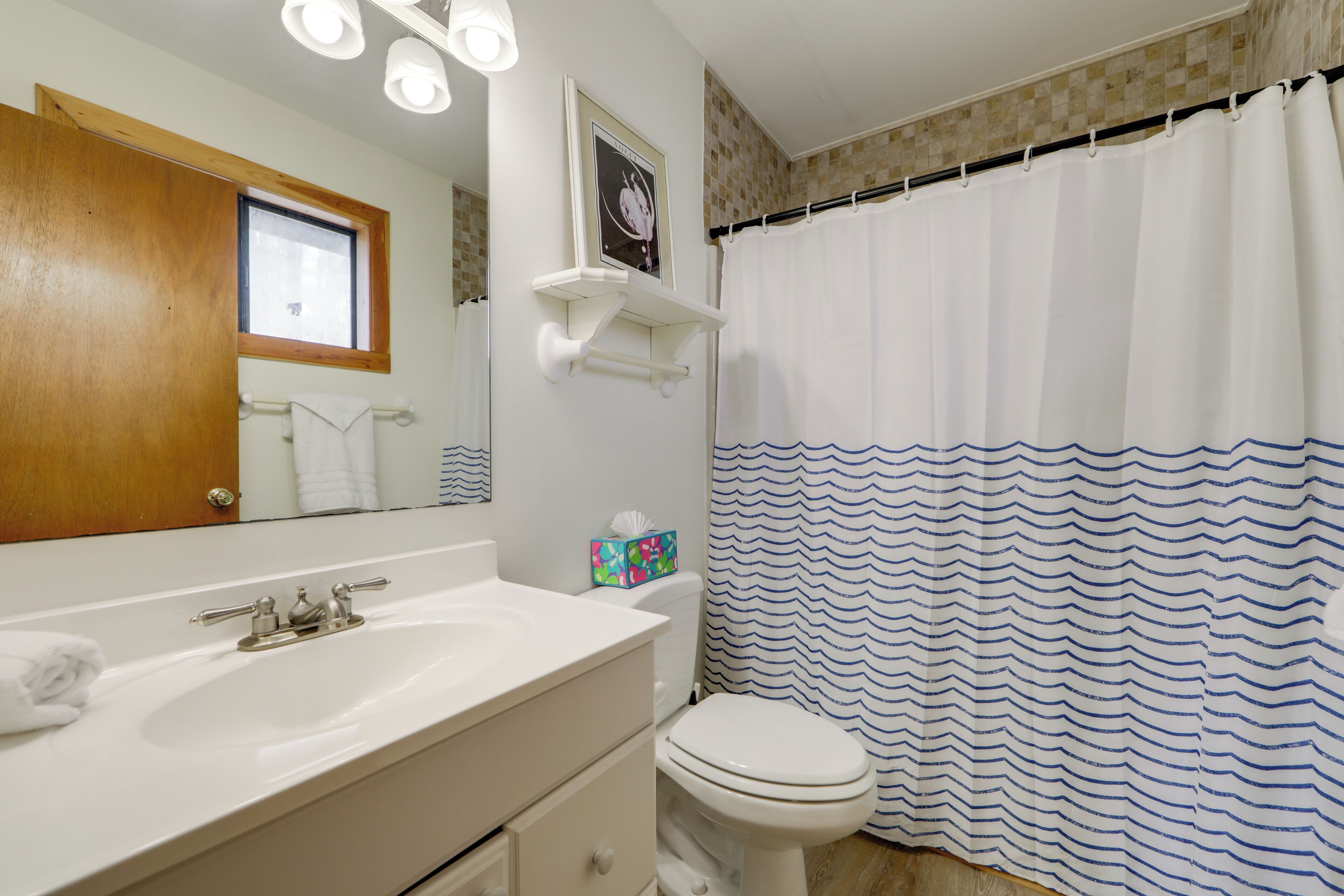 Un baño con lavamanos blanco, inodoro, espejo y cortina de ducha con un estampado azul ondulado.