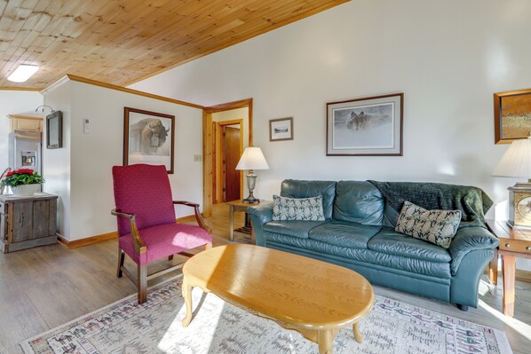 A living room with a wooden ceiling, a blue leather sofa with patterned cushions, a wooden coffee table, and a red armchair. - Dog-friendly Cabin 6 Mi to Cataloochee Skiing! (Maggie Valley)
