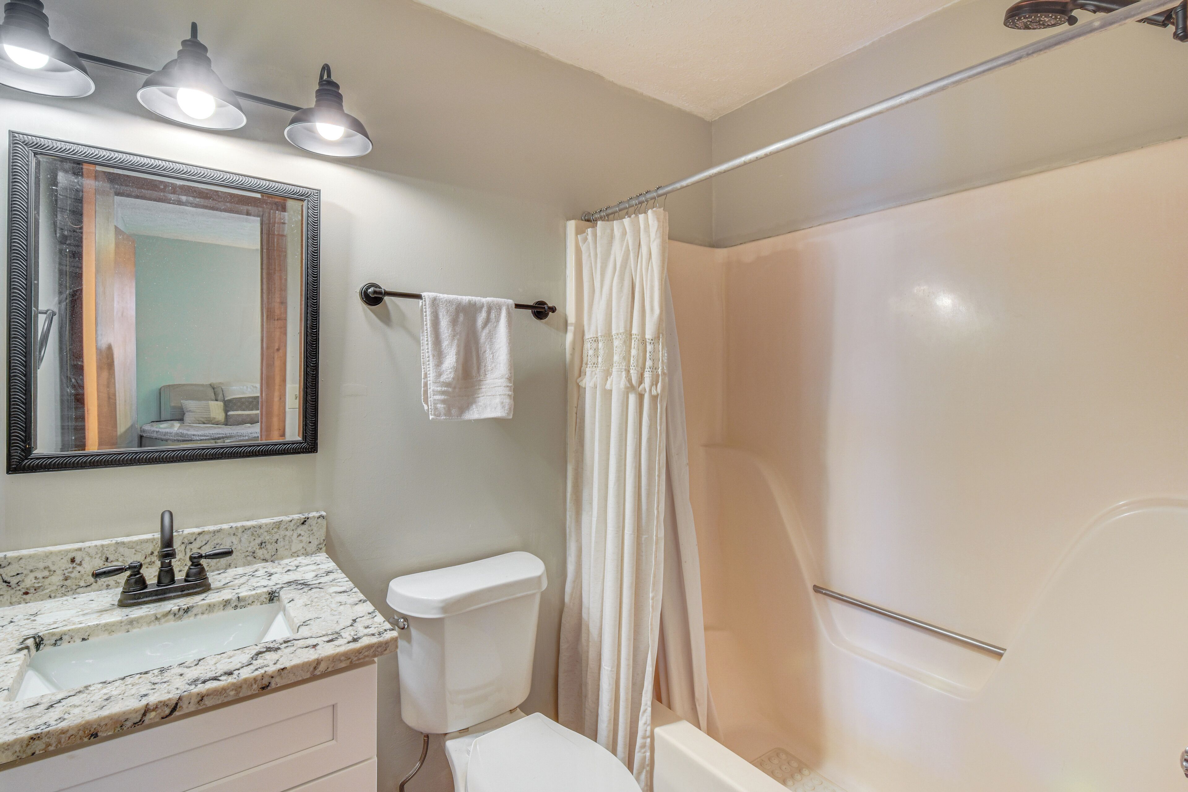 Une salle de bain avec un lavabo en marbre, des toilettes, une douche avec un rideau et un miroir avec éclairage.