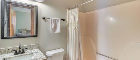 Une salle de bain avec un lavabo en marbre, des toilettes, une douche avec un rideau et un miroir avec éclairage.