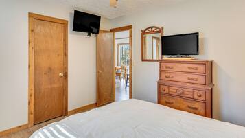 A bedroom with a bed, wooden dresser, two wooden doors, a television mounted on the wall, and a mirror above the dresser.