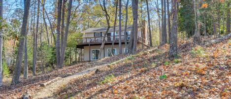 A two-story house with a balcony, surrounded by a forested area with fallen leaves.