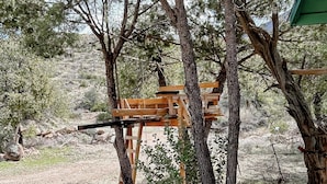 A wooden structure supported by trees, likely a rustic outdoor seating area or a simple shelter.