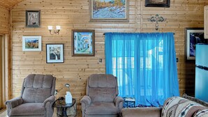 A cozy wooden cabin interior with two armchairs, a small table, and a sofa.