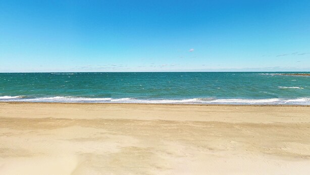 Une plage avec une eau d’un bleu limpide et un rivage sablonneux.