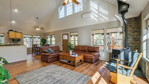A spacious living area with a fireplace, leather sofas, a wooden coffee table, and a large window providing natural light. - Pet-friendly Blue Ridge Cabin: Wraparound Deck! (Happy Jack)