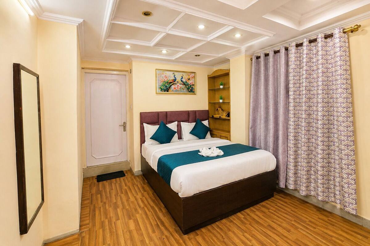 Een hotelkamer met een bed, een deur, een plafond met inbouwspots en een kamerbreed gordijn met patroon.