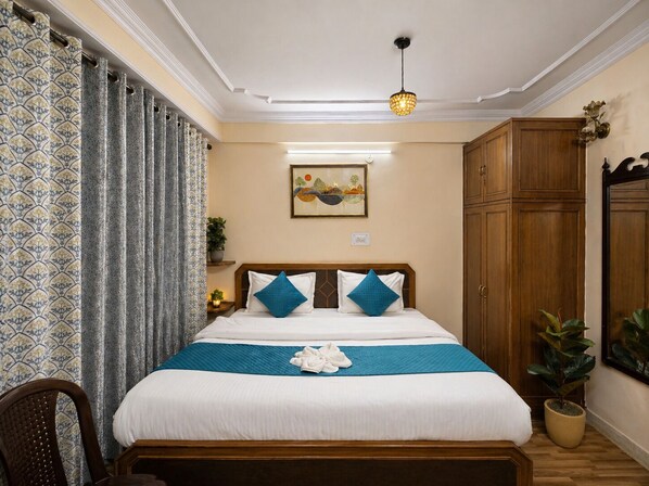 Quarto de hotel com cama, mesa de cabeceira, planta em vaso, guarda-roupa de madeira e um quadro na parede.