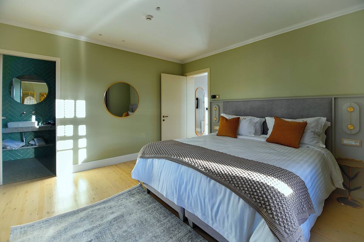A bedroom with a large bed, a bedside table, a mirror, and a door leading to a bathroom.