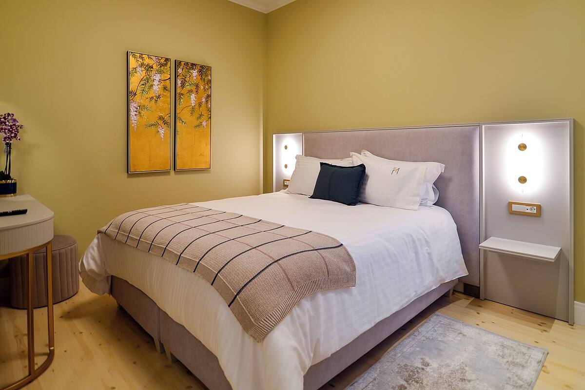 A neatly arranged bedroom with a large bed, bedside lamps, and two wall-mounted paintings.