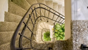 A spiral staircase with a metal railing and a potted plant at the bottom. - Megaro Gioule (Voio)
