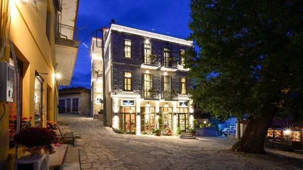 A stone-paved courtyard with a two-story building featuring balconies and outdoor seating. - Megaro Gioule (Voio)