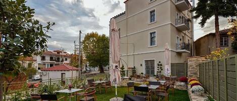 An outdoor patio with multiple tables and chairs, surrounded by a stone wall and a building with balconies.