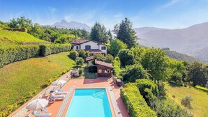 Eine Villa mit Swimmingpool, umgeben von üppiger Vegetation und Bergen im Hintergrund.