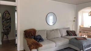 Een woonkamer met een beige bank, een ronde spiegel en een vloerkleed met een patroon.