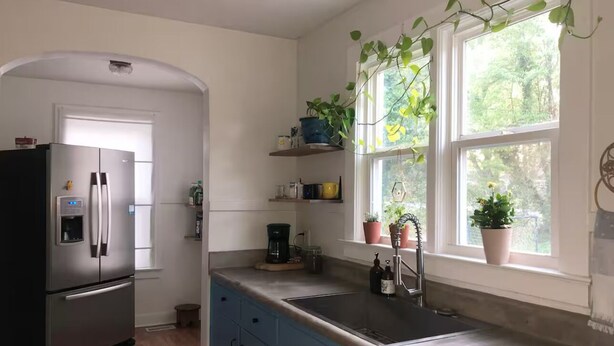 Een moderne keuken met een roestvrijstalen koelkast, een dubbele spoelbak en een raam met plantenpotten.