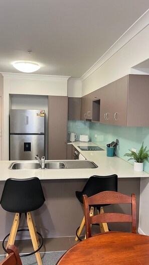 A compact kitchen with a built-in refrigerator, double sink, and a small dining area with a wooden table and two chairs.