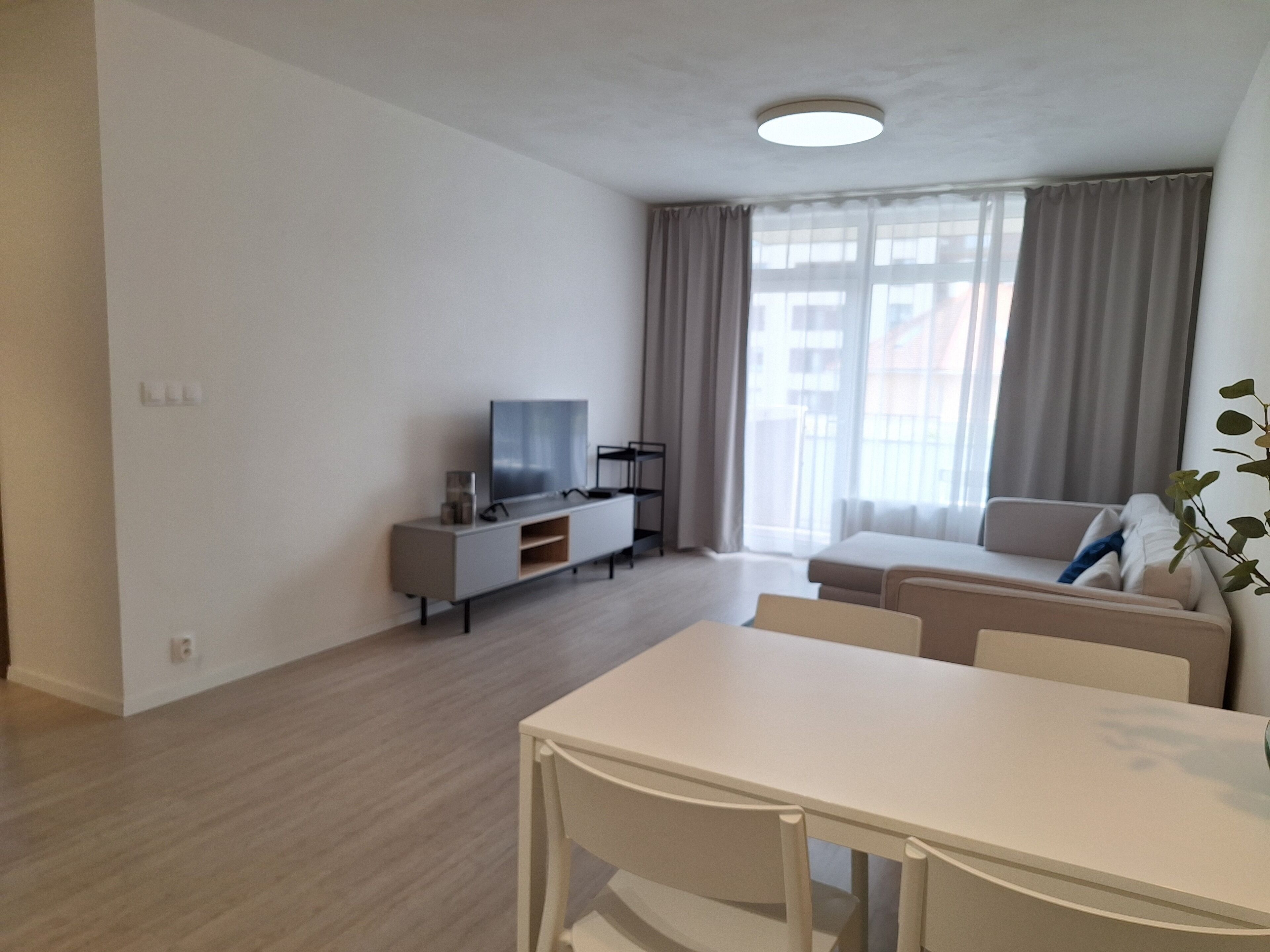 A modern living room with a white sofa, a TV on a stand, and a dining table with chairs.
